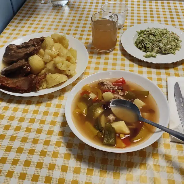 Talerz zupy z warzywami obok drugiego dania i kompotu